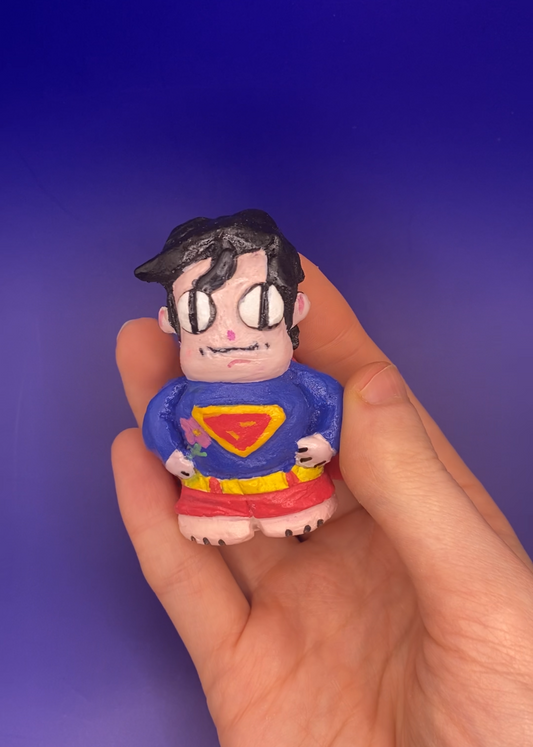 Hand holding a small figurine of a character in a superhero costume against a blue background