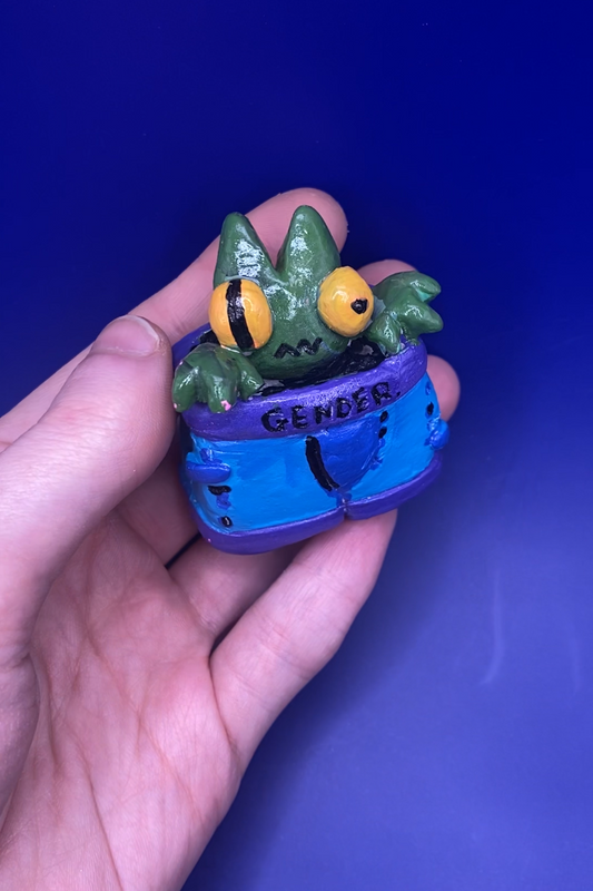 Small figurine of a creature with a blue underwear held in a hand against a blue background